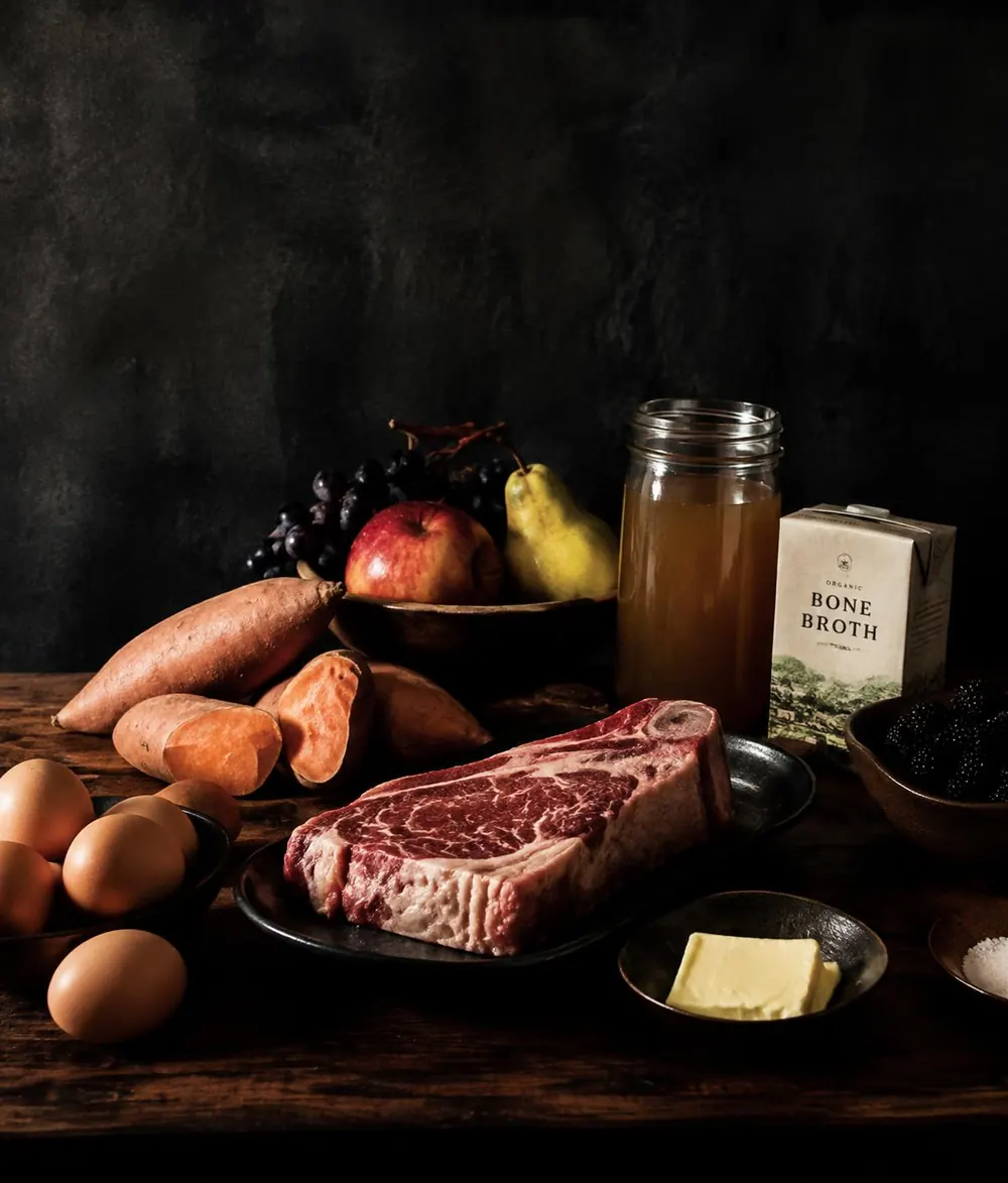 Carne, ovos, batata-doce, frutas e manteiga sobre mesa de madeira